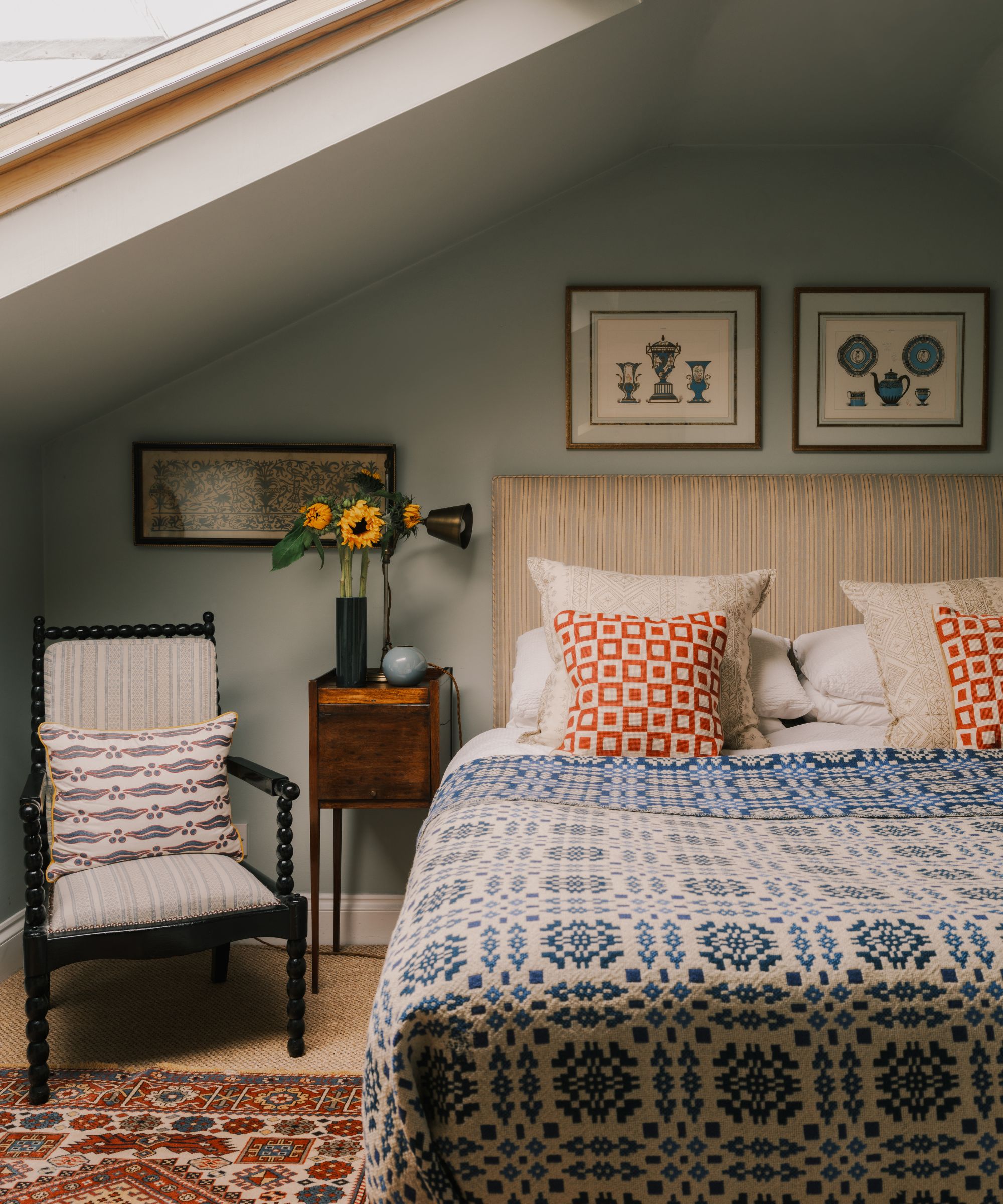 Vintage bedroom with pale blue walls, striped headboard with vintage quilt, mahogany nightstand, bobbin chair and Persian rug on the floor