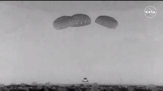 a black and white view of a capsule descending under parachutes. a nasa logo is at upper right as the broadcast ran on nasa television