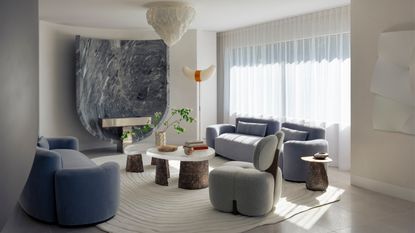 Image of a living room with a cream and light blue color scheme. There is a nesting coffee table in the center of the room with two blue velvet sofa across from each other and a gray accent chair.