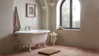 freestanding bath with claw feet on brick terracotta floor tiles in bathroom with arched window