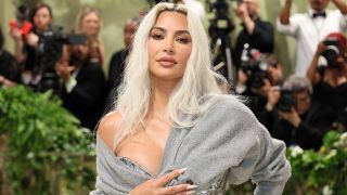 Kim Kardashian in sheer John Galliano dress with grey sweater at 2024 Met Gala.