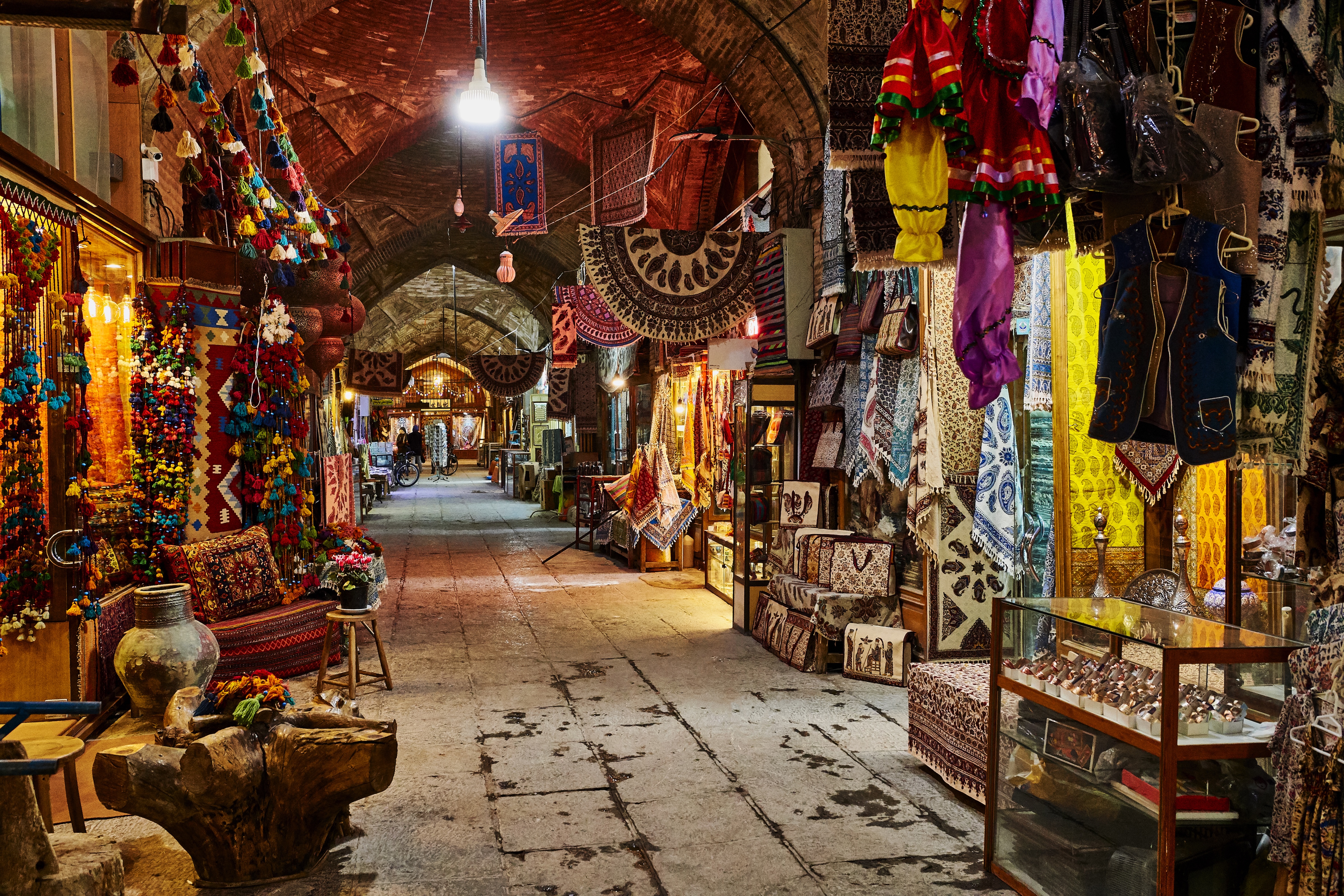 Stone street in a bazaar with colourful wares hanging from the walls and vaulted ceiling