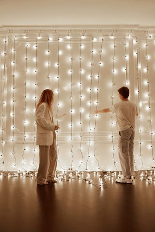 People adjusting drape of Christmas lights on wall