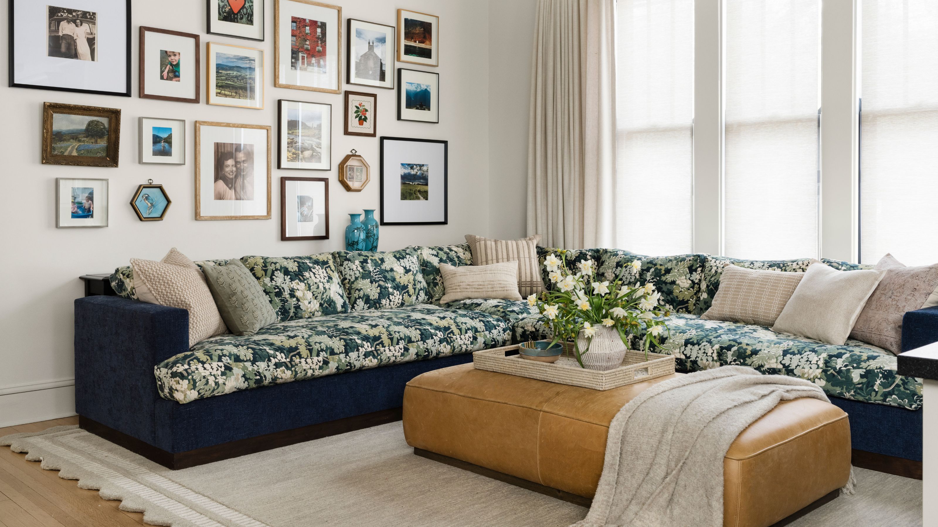a neutral family room styled with a large navy sectional with green botanical print cushions, a leathe ottoman and an eclectic gallery wall