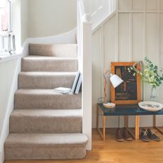 Neutral hallway with hard flooring and a small table, leading to a carpeted staircase with white banister