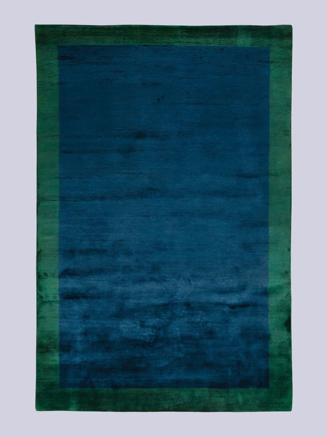 A bright blue mohair rug with a green border from The Rug Company