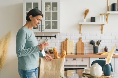 Woman at home with back of groceries frustrated while looking at receipt from supermarket