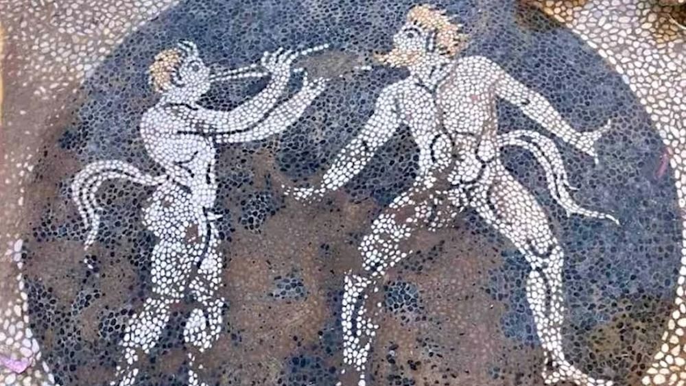 A colorful mosaic of two men with tails, horns and pointed ears dancing.