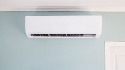 Interior wall mounted air conditioner on a light gray-blue wall with corner of white doorway in shot on bottom right