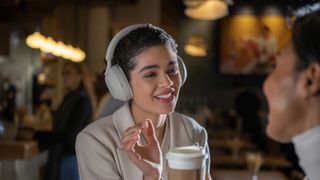 Woman wearing white Sony WH-1000XM5 headphones in busy coffee shop