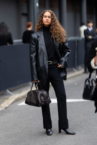 Sarah Lysander wears a black turtle neck sweater, a black belt, black high waist trousers, black leather heeled ankle boots, a dark brown leather bag and a black leather oversized blazer outside Tod's show during the Milan Fashion Week Menswear Spring/Summer 2025 on September 20, 2024 in Milan, Italy.