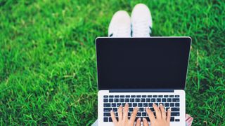Person with laptop on grassy field
