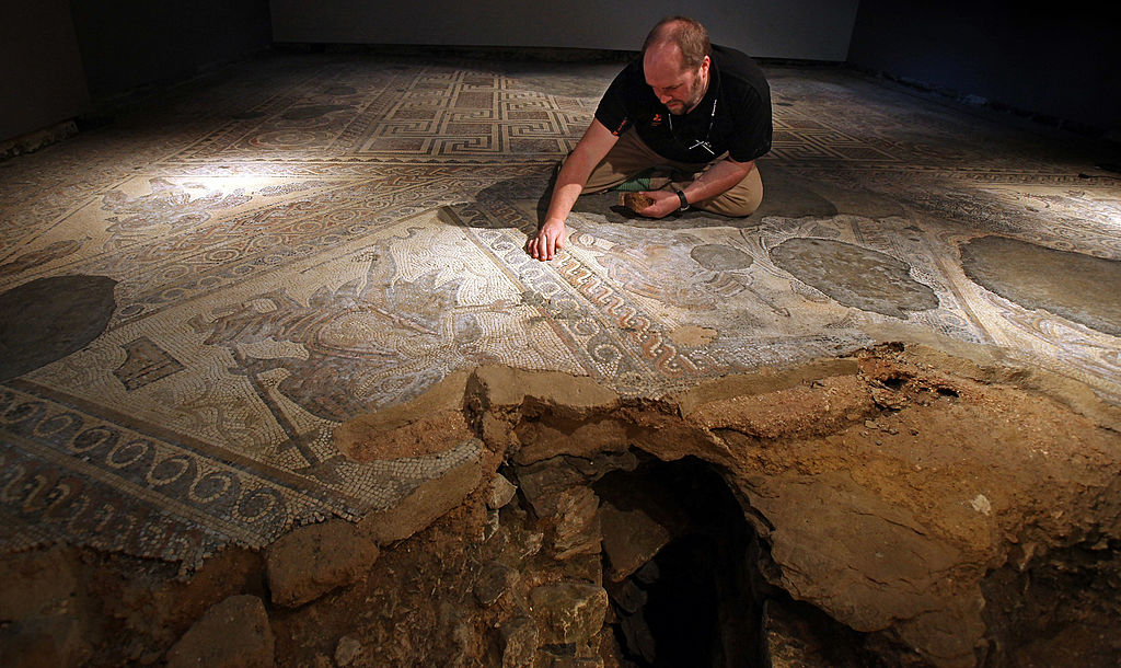 A man crouches over a large carved flooring in a dimly lit room.
