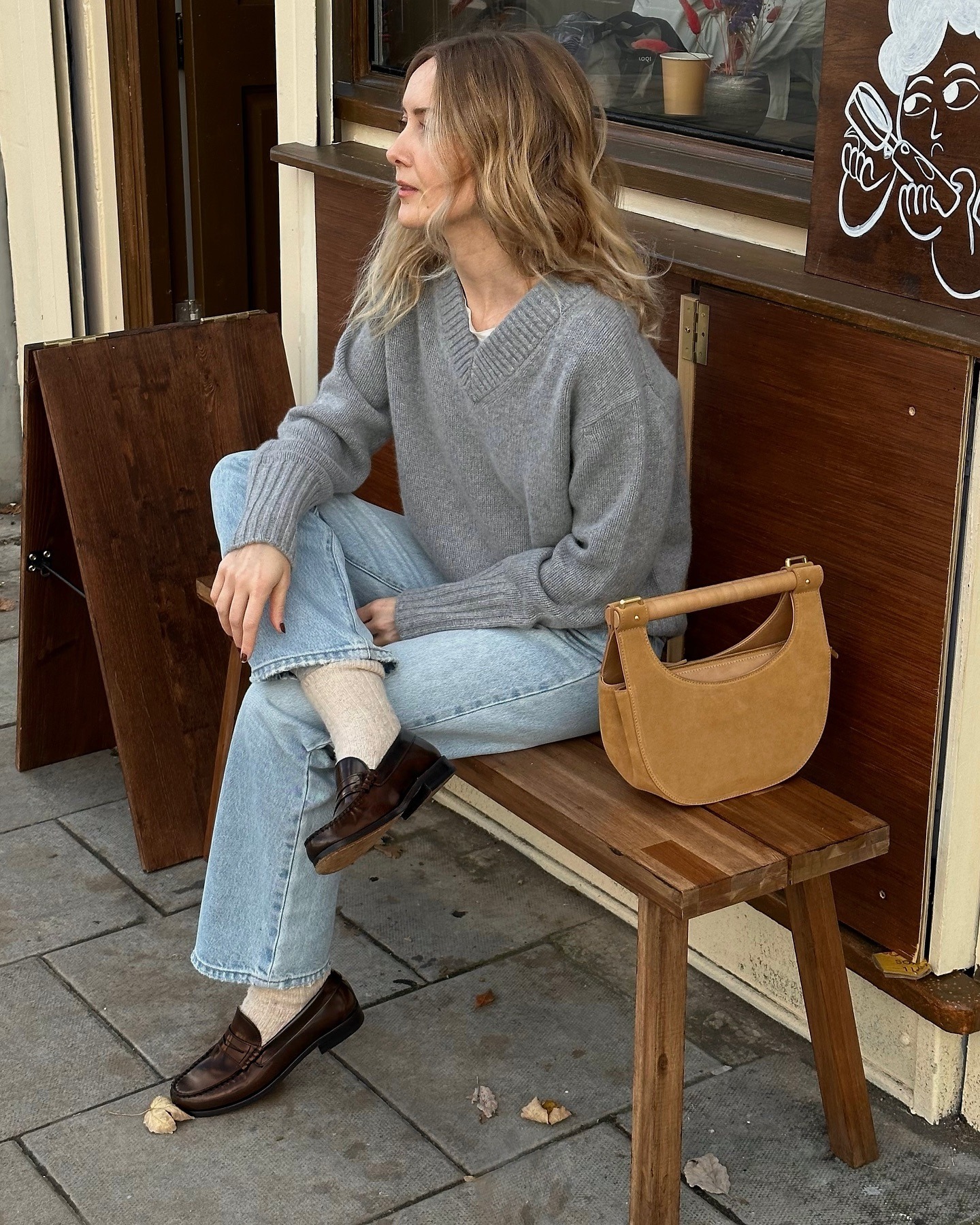 Chloe wears a grey v-neck jumper, blue jeans and loafers