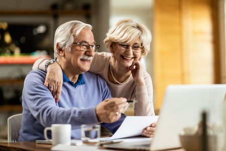 A couple looks happily at a piece of paper and a computer. 