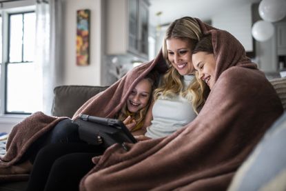 Woman and two children under a blanket using digital tablet