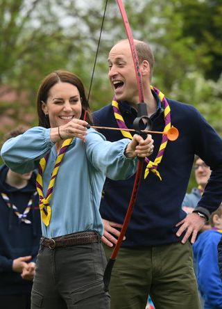 Kate Middleton using a bow and arrow as Prince William laughs