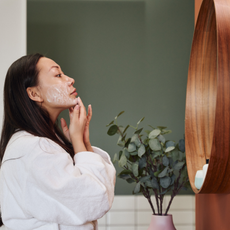 Woman in white robe applying skincare in a mirror