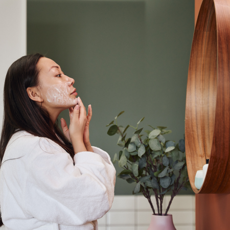 Woman in white robe applying skincare in a mirror