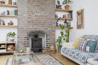 White living room with exposed brick fireplace, open shelving in alcoves and white sofa covered with blue and white throw