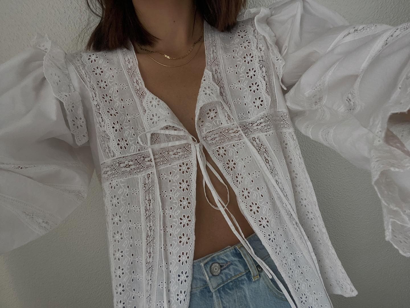 Influencer wears a white tie-front blouse with embroidery partially unbuttoned and styled with jeans.