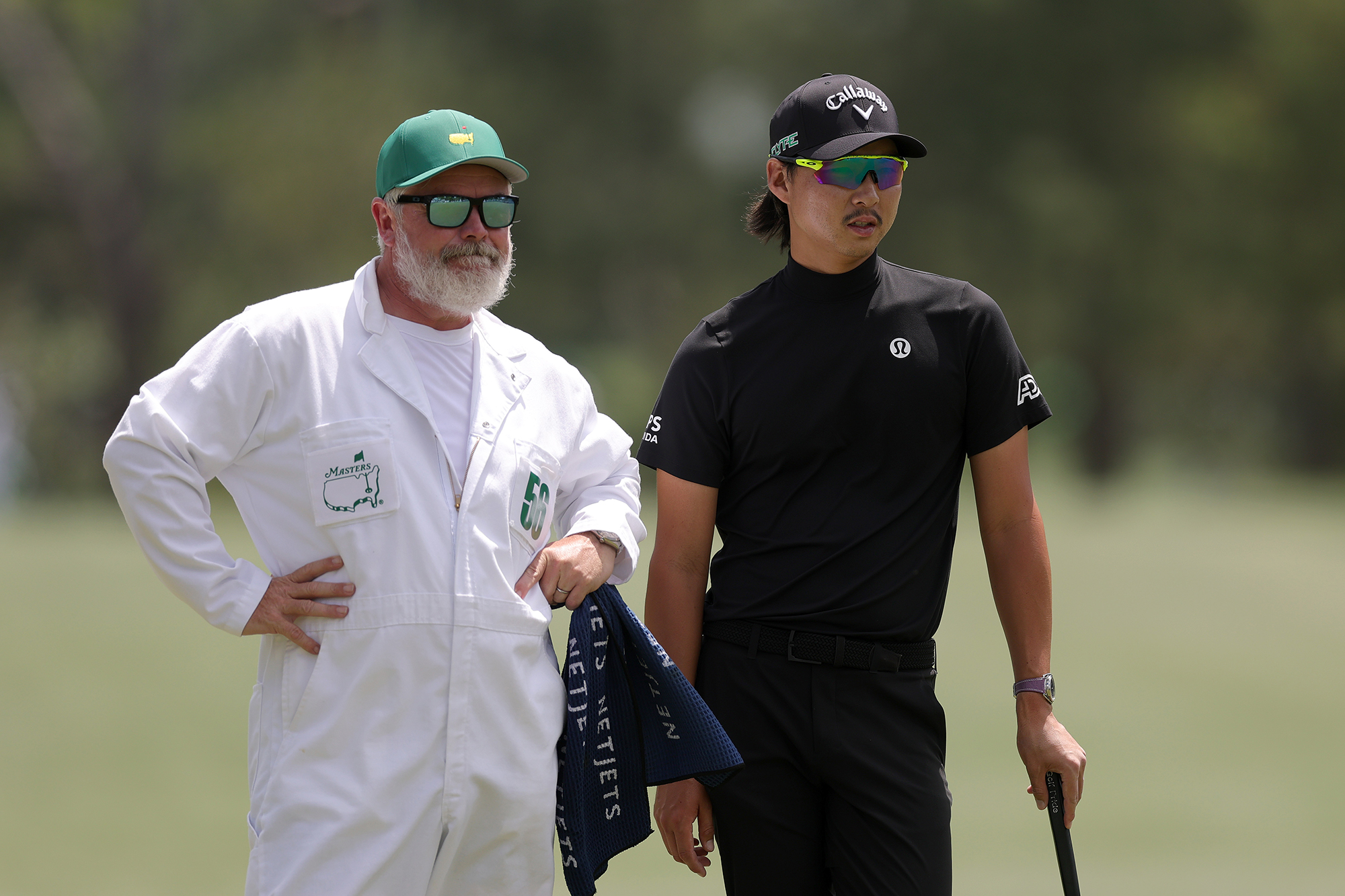 Min Woo Lee talking to his caddie, who is wearing the traditional white boiler suit, at the Masters in 2025