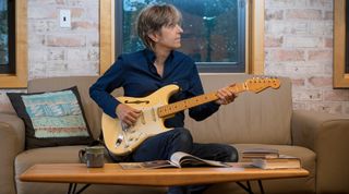 Eric Johnson plays one of his signature Fender guitars while seated on a couch