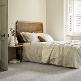 Double bed on top of grey carpet with wooden headboard and linen blankets