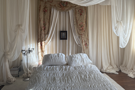 A bedroom draped in floating, beige, white, and floral textiles, with a chrome candlelabra and a framed picute on its back wall.