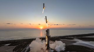 A rising sun on the horizon of the sea makes way for a tall tower among the flat, grassy sand dunes of the beach, and three boosters, engines lit, descending sequentially toward the tower.