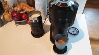 En svart Nespresso Vertuo Next står på en vit bänk och har precis bryggt en kopp kaffe.
