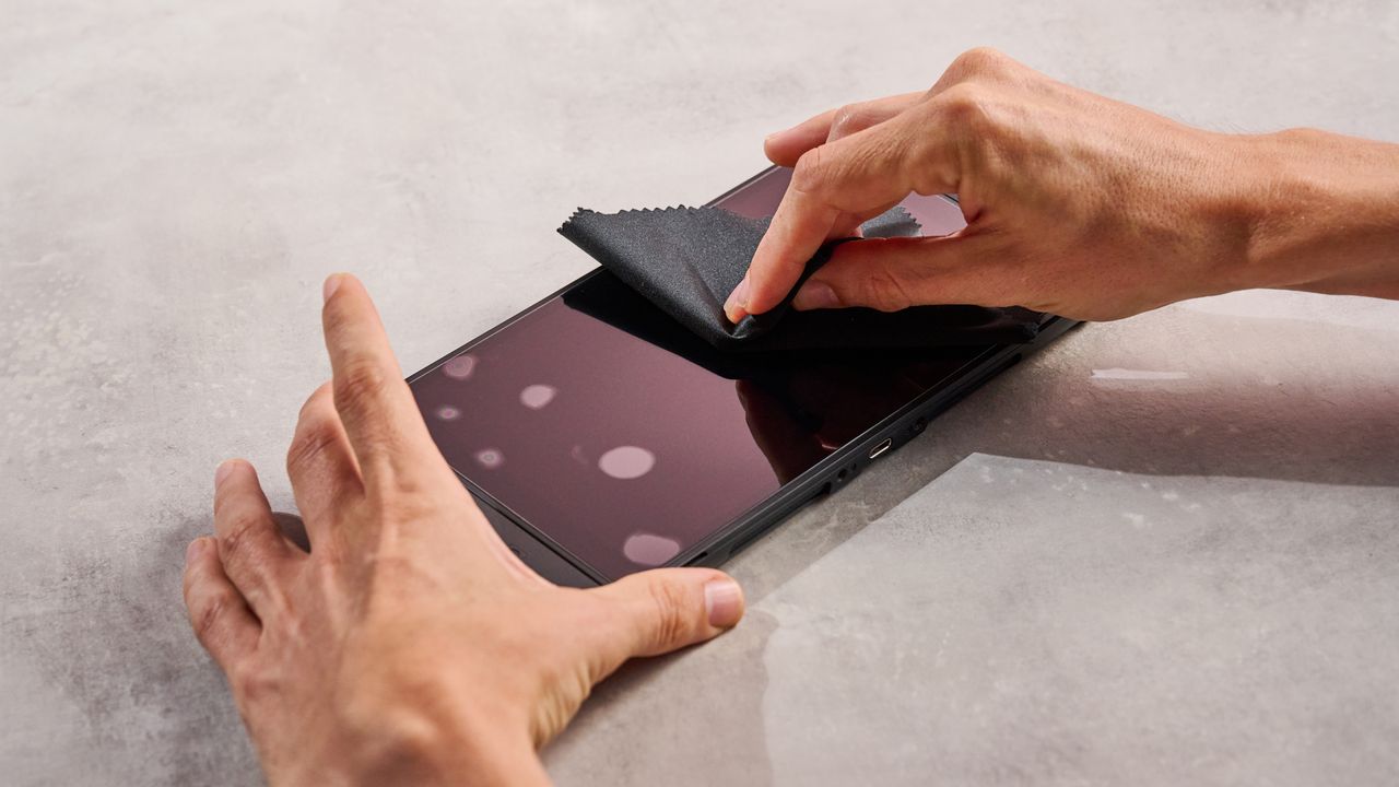 A man puts pressure on the Snakebyte Starter Kit S2 screen protector using a microfiber to attempt to remove bubbles from under it.