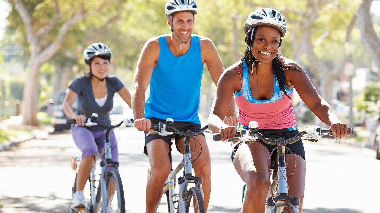 Two women and a man cycling down a tree-lined street on bikes