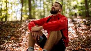 Male runner wearing headphones pausing in woods