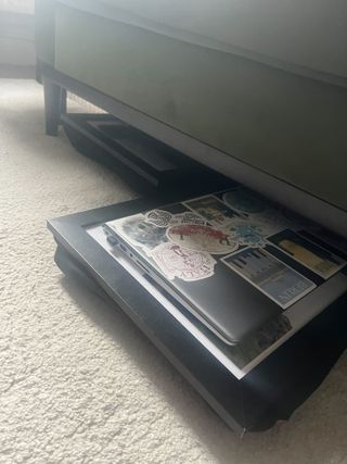 Two lap trays under a green sofa on a white rug, one with a grey laptop on it