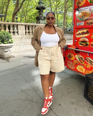 Aniyah wears long shorts white tank and brown blazer with red and white Nike shoes