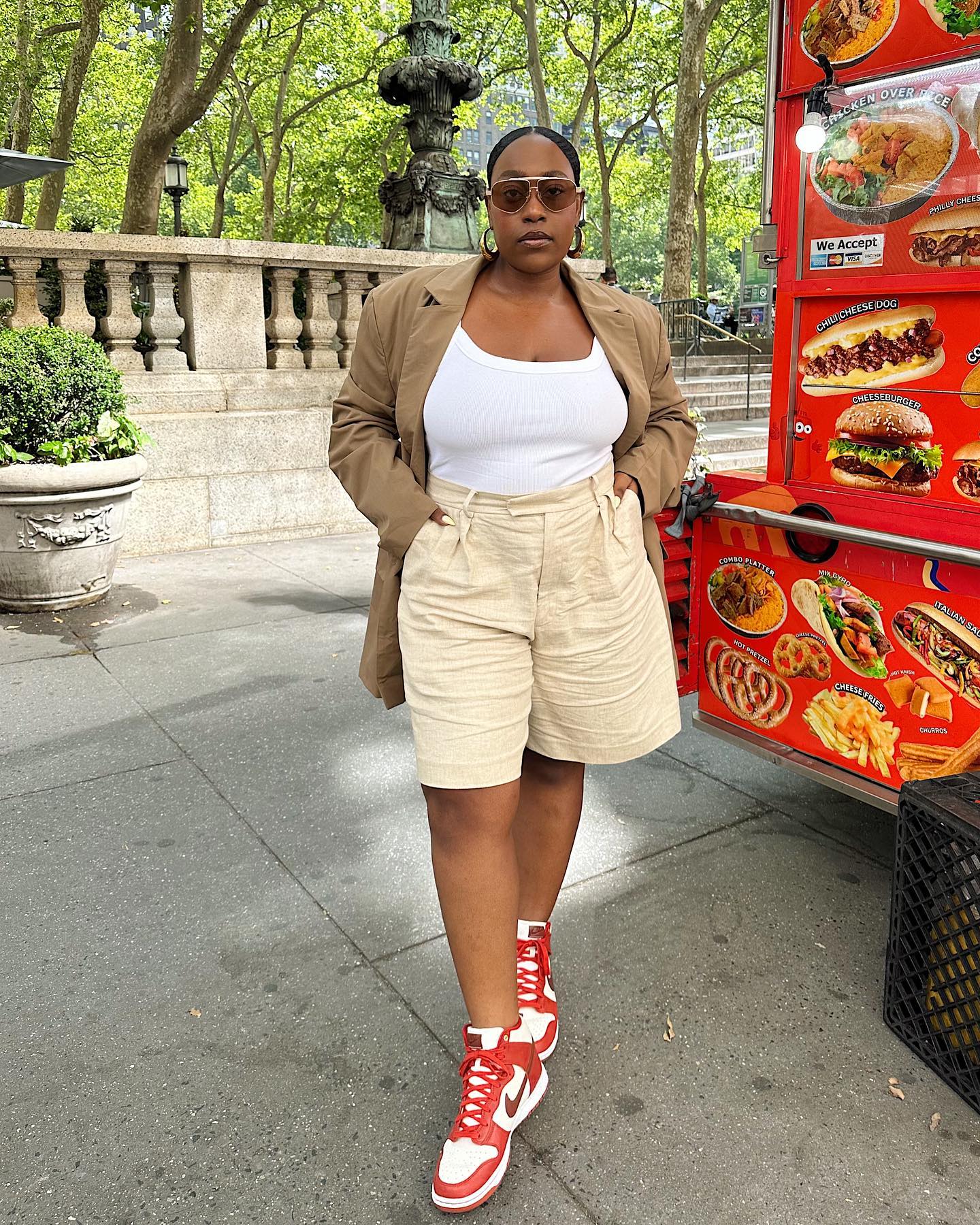 Aniyah Morinia wears long shorts, a white tank, and a brown blazer with red-and-white Nike shoes
