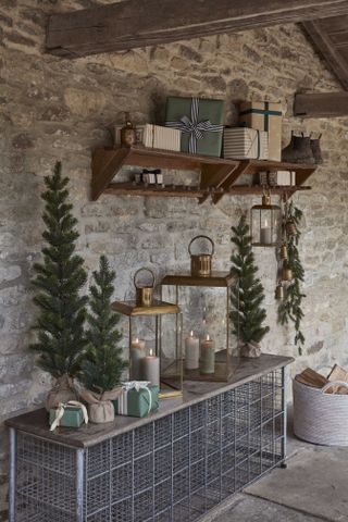 exterior of house with Christmas decorations, lanterns, presents on a shelf, wood and wire bench, basket with logs, mini trees