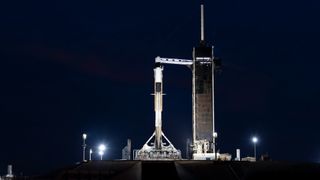 a white rocket standing upright on a launch pad at night