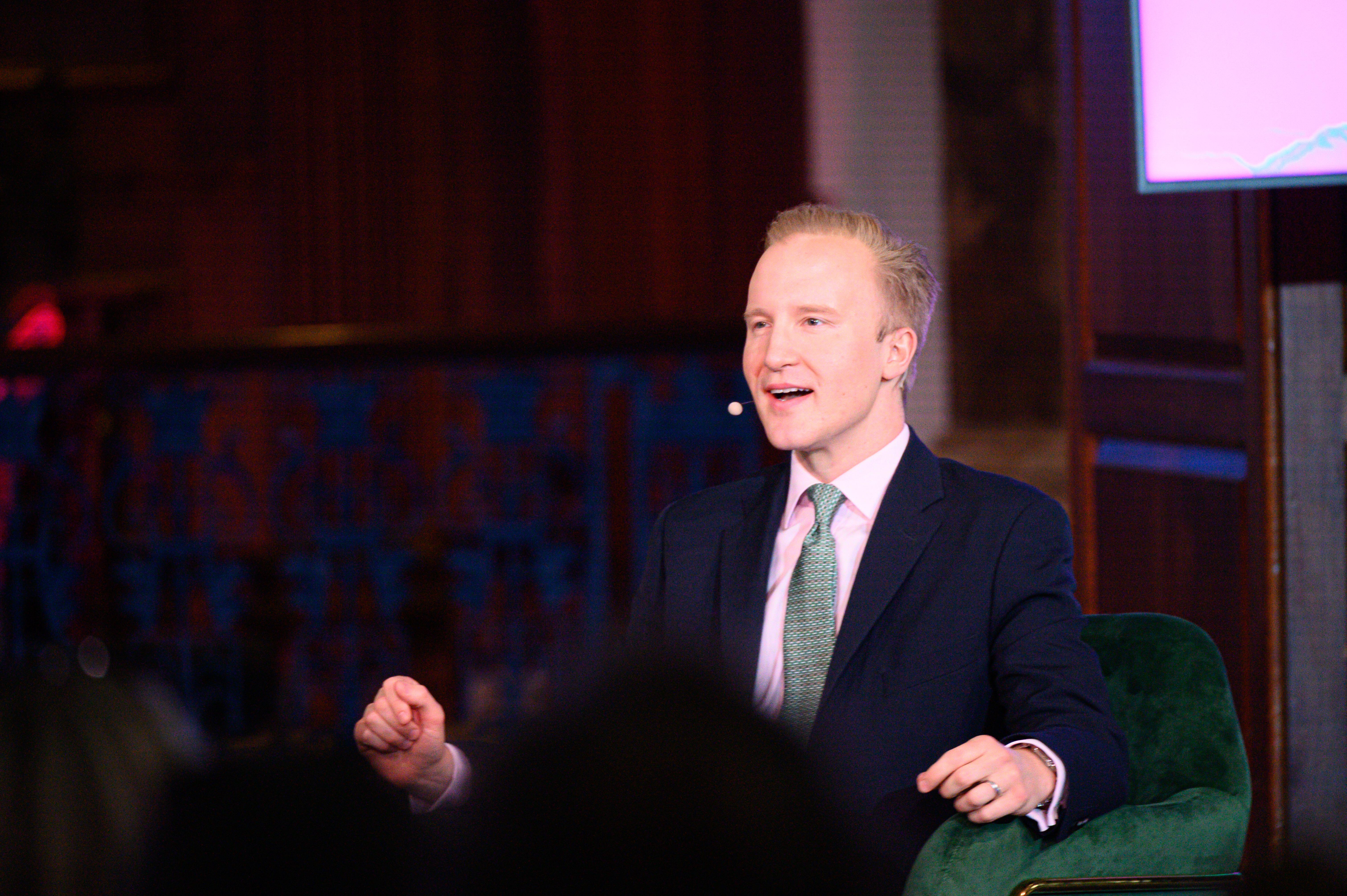 William Hanson in conversation at an event, wearing a dark suit and green tie