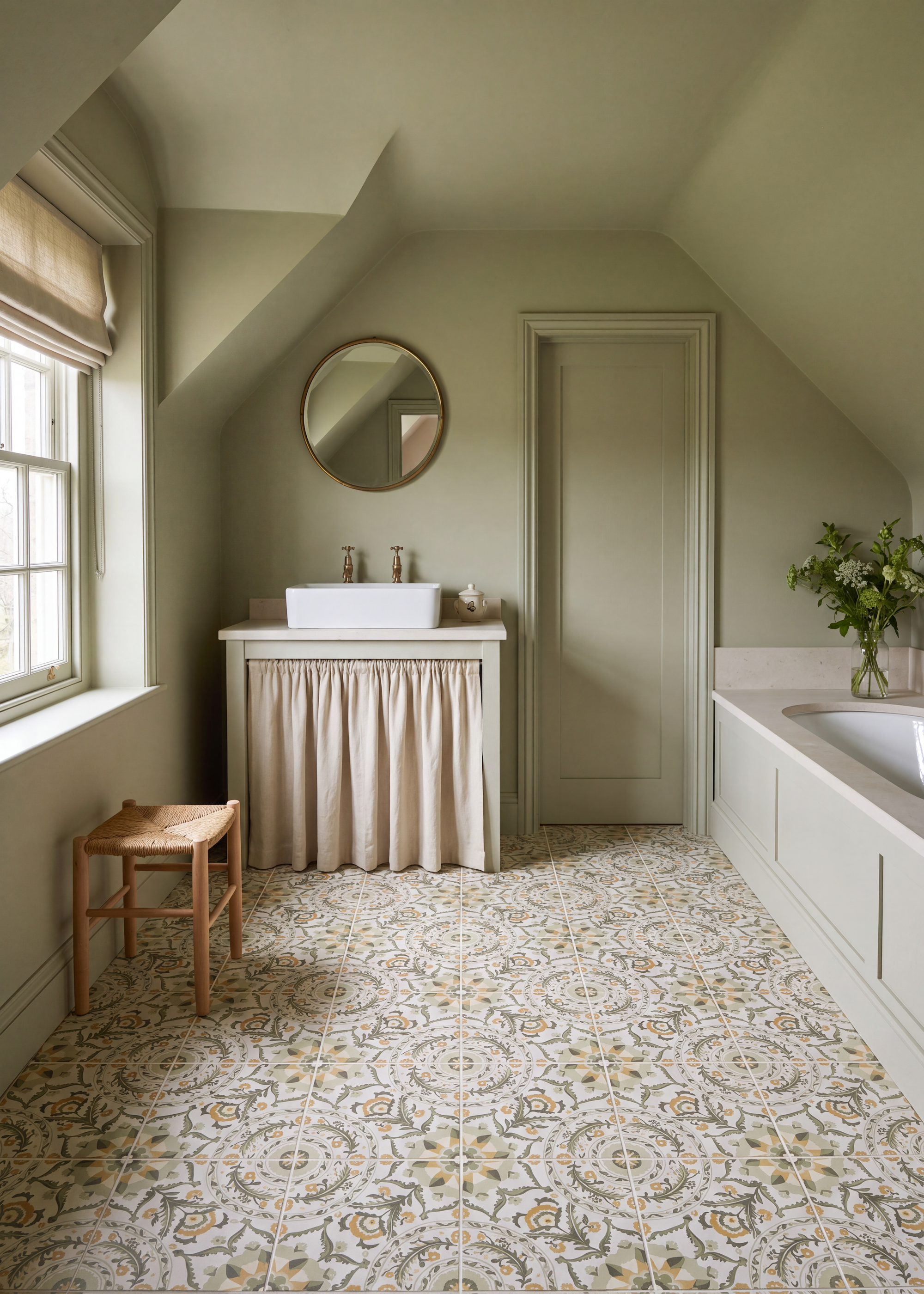 A calm, soothing bathroom scheme with sage green walls, patterned floor tiles in earthy neutrals and brass details on the basin and mirror