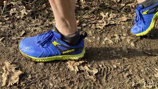 Closeup of Inov8 TrailTalon all-terrain running shoes being worn on muddy trail