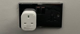 The Meross Smart Wi-Fi Plug Mini MSS110 plugged into an electrical socket on a gery wall