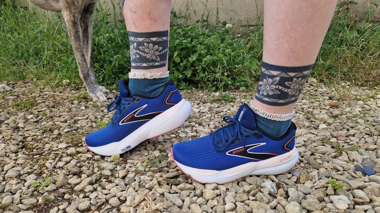 A pair of blue Brooks Glycerin 21, modelled on a gravel path. In the background we see grass and a dog&#039;s legs.