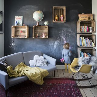 Childs bedroom with crate shelving on chalk board painted wall with couch and chair