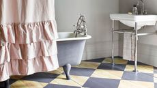 Freestanding gray tub in whimsical bathroom with ruffled shower pink curtain and gray checkered floor paint on hardwood