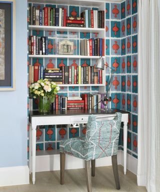 Colorful nook decorated with blue and red patterned wallpaper, bookshelf, small desk and chair