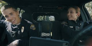 Two police officers (Brandon Larracuente as Alex Diaz and Troian Bellisario as Traci Harmon) laugh in the front seat of a police car in 'On Call.'