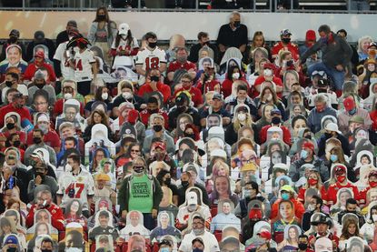 Fans wearing masks sit by cardboard cutouts at the Super Bowl.