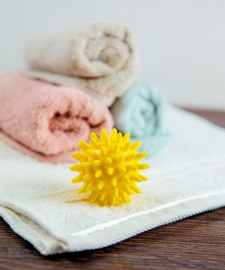 A plastic dryer ball on a white towel in front og a stack of rolled colorful towels